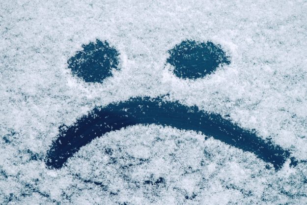 Sad smiley emoticon face drawn on snow covered glass winter season sadness concept