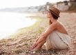 Calm woman sitting alone on a sand evening beach, sad and pensive