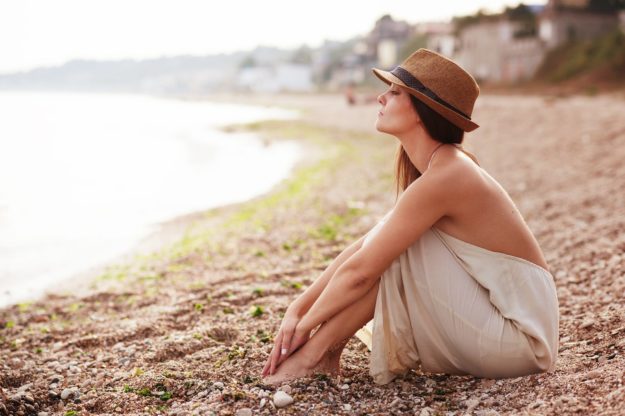 Calm woman sitting alone on a sand evening beach, sad and pensive