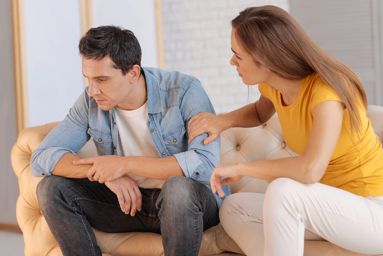 Something wrong. Attentive caring kind wife looking worried while sitting near her unhappy tired husband and trying to find out the reason for his bad mood