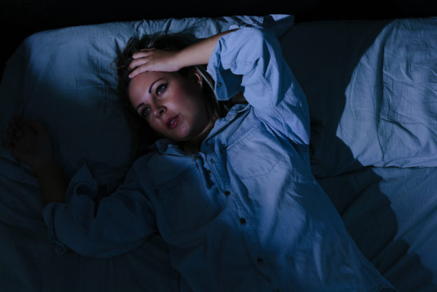 Sleep disorder insomnia. Young blonde woman lying on the bed awake