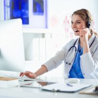 Young practitioner doctor working at the clinic reception desk, she is answering phone calls and scheduling appointments