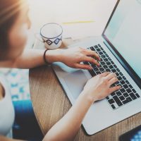 Closeup of woman surfing web at living room on modern computer while sitting at the wooden table.Female hands typing on laptop keyboard.Concept of young modern people using mobile devices at home